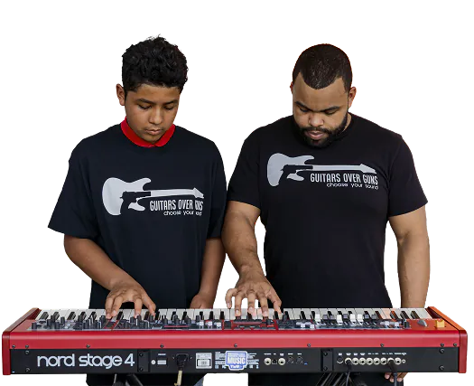 A boy and a man standing side by side playing a red Nord Stage 4 keyboard together, both wearing black t-shirts that say 'GUITARS OVER GUNS choose your song' with a guitar graphic.